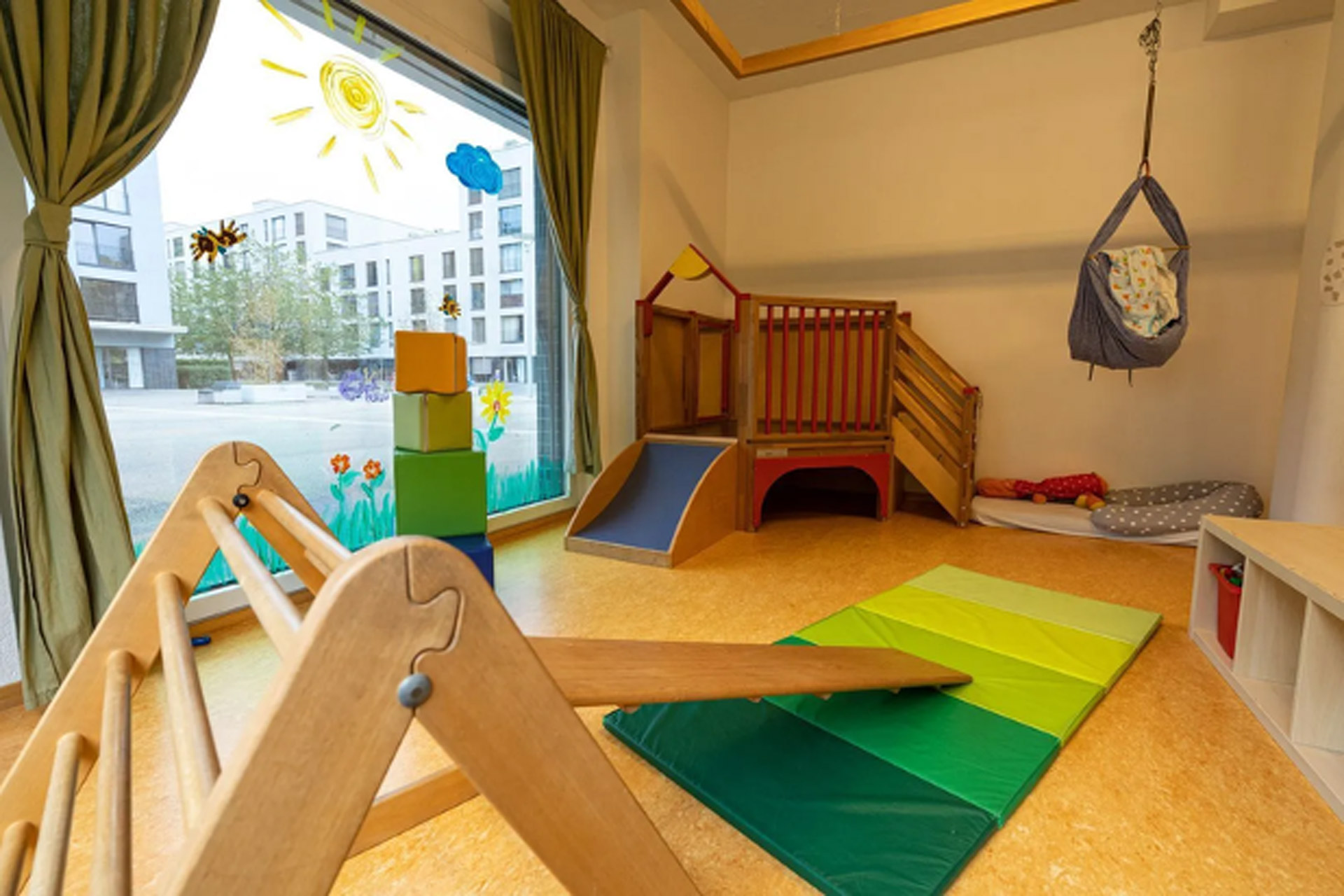 Kita kidsco Binzallee Bewegungsraum der Kita mit einer Fensterfront und Holzspielzeug und Holz Mobiliar