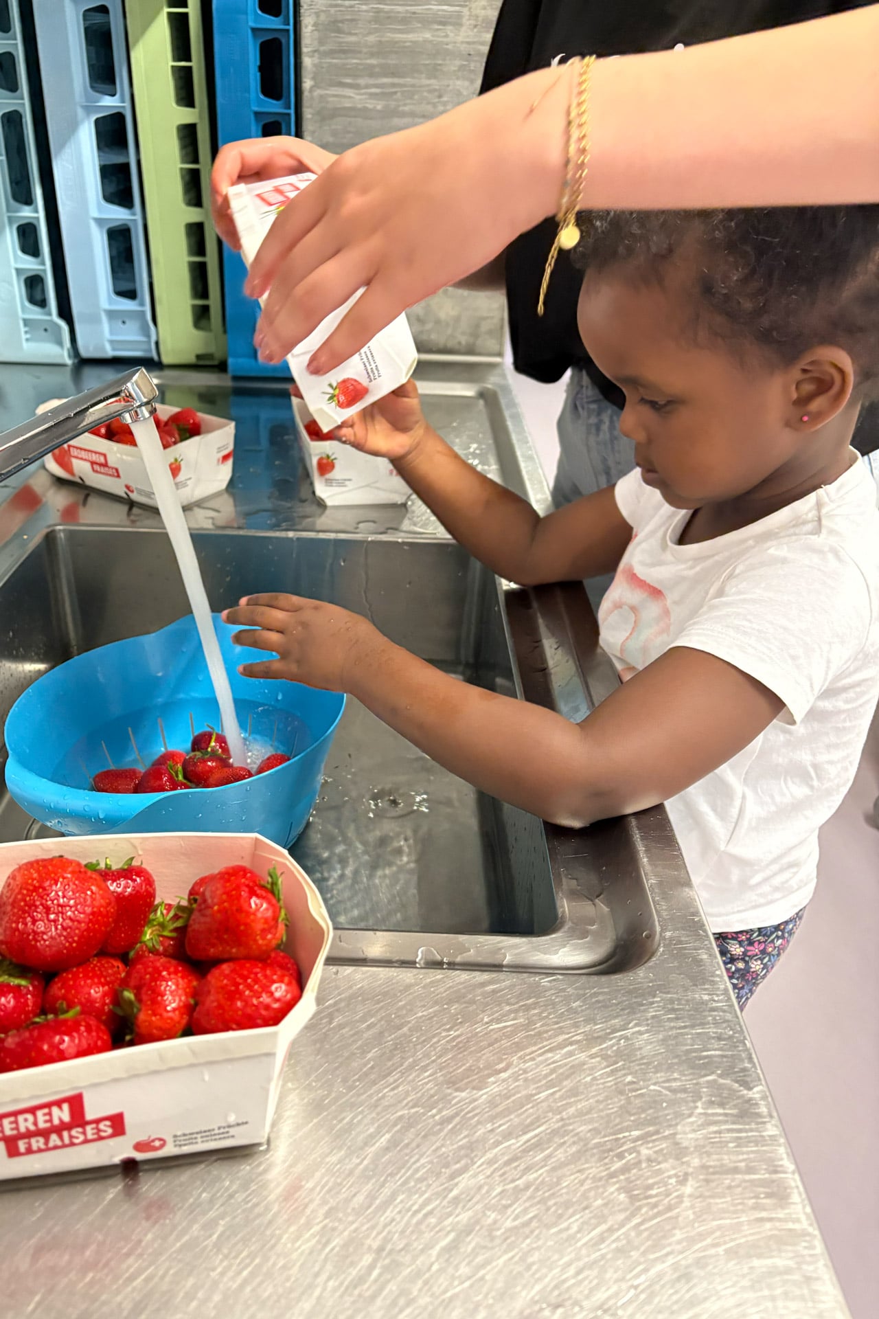 Kita kidsco Letzibach Betreuerin unterstütz Kind beim Waschen von Erdbeeren